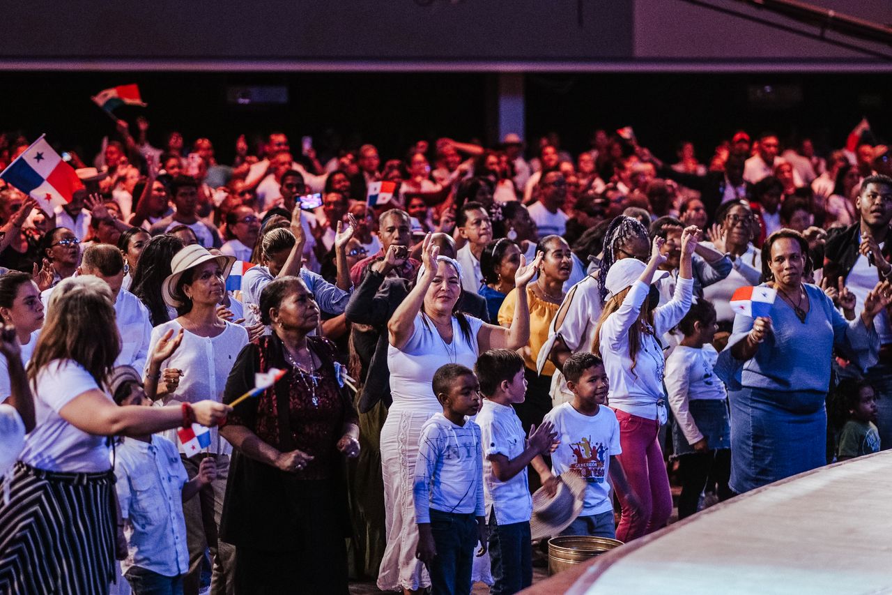 A lively crowd in a festive ceremony waving flags indoors with vibrant energy.